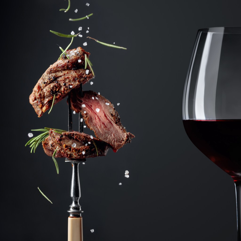 steak bites on fork with glass of red wine